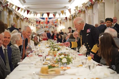 En el mismo evento, el rey Carlos III conversa animadamente con sus compañeros de mesa antes de sentarse a tomar el té.