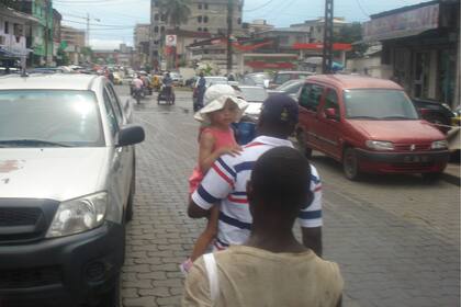 En en mercado central en Douala, junto a su hija en brazos, detrás un changarín lo secunda