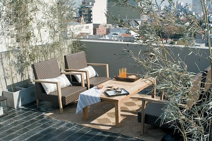 En esta amplia terraza se logró un rincón de relax con una alfombra de yute que sirve delimitar el espacio. Los tonos tierra de los sillones y la mesa de teca se complementan con las plantas en macetas de cemento