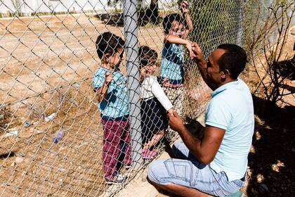 En esta foto de archivo tomada el 10 de septiembre de 2017, el refugiado sirio Ammar Hammasho saluda a sus hijos de los que fue separado debido al conflicto, mientras se reúnen en el campo de refugiados de Kokkinotrimithia