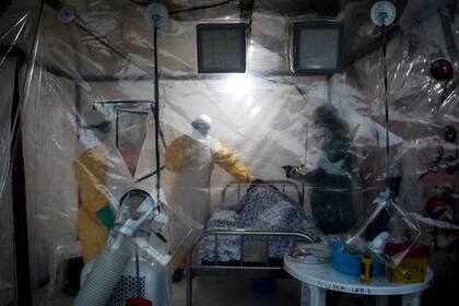 En esta foto de archivo tomada el 15 de agosto de 2018, tres trabajadores médicos controlan a un paciente con ébola en un Biosecure Emergency Care Unite (CUBE) en Beni