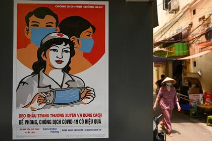 En esta foto de archivo tomada el 29 de abril de 2020, se ve un cartel de propaganda sobre la prevención de la propagación del nuevo coronavirus en una pared mientras una mujer pasa caminando por una calle en Hanoi
