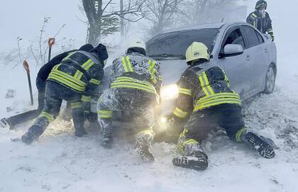 En esta foto proporcionada por el Servicio de Emergencia de Ucrania, trabajadores de emergencia ucranianos intentan empujar un automóvil atrapado en la nieve en la autopista de la región de Odesa, Ucrania, el lunes 27 de noviembre de 2023. 