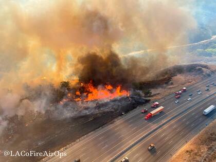 En esta fotografía aérea difundida por Operaciones Aéreas del Departamento de Bomberos del condado Los Ángeles se ve a vehículos que transitan por la Interestatal 5 cerca de un incendio forestal al norte de Castaic, California