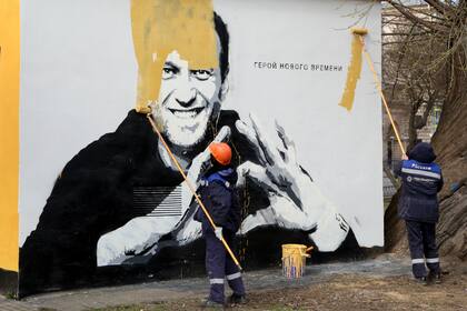 En esta imagen de archivo del 28 de abril de 2021, trabajadores municipales pintan sobre una imagen del encarcelado líder opositor ruso Alexei Navalny en San Petersburgo