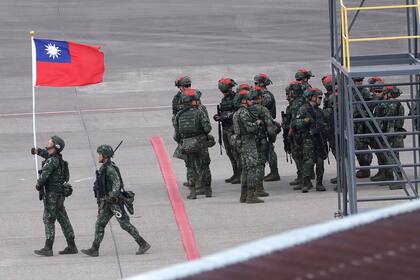 En esta imagen de archivo, un soldado taiwanés sostiene una bandera de Taiwán cerca de un grupo de soldados con marcas rojas en sus cascos porque se harán pasar por enemigos durante las maniobras anuales Han Kuang, que simulan un ataque a un aeródromo, en el aeropuerto internacional Taoyuan, en Taoyuan, Taiwán, el 26 de julio de 2023. (AP Foto/Chiang Ying-ying, archivo)