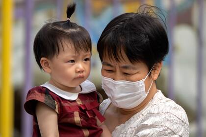 En esta imagen de archivo, una mujer con mascarilla lleva una niña en brazos en un parque público en Pekín, el 1 de junio de 2023.