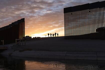 En esta imagen del jueves 10 de junio de 2021, un par de familias de migrantes brasileños pasan por una apertura en el muro fronterizo para llegar a Estados Unidos después de cruzar desde México hacia Yuma, Arizona, para solicitar asilo. (AP Foto/Eugene Garcia, Archivo)