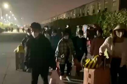 En esta imagen extraída de un video y publicada por Hangpai Xingyang, gente con maletas sale de un complejo de Foxconn en Zhengzhou, en la provincia central china de Henan, el sábado 29 de octubre de 2022. Los trabajadores en una planta de Foxconn en laciudad central china de Zhengzhou parecían haber abandonado el recinto para evitar restricciones asociadas al COVID-19. (Hangpai Xingyang via AP)