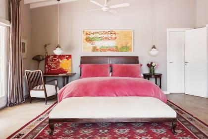 En este espacio, la cama con respaldo en madera y cuero se acompaña con dos lámparas colgantes de opalina de los años 60; para darle mayor protagonismo, una cómoda banqueta a modo de pie de cama y una alfombra de Marruecos
