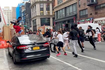 En este fotograma, un individuo salta sobre un auto mientras un grupo de personas corre por la calle en Broadway, cerca de Union Square, el viernes 4 de agosto de 2023. (AP Foto/Bobby Calvan)