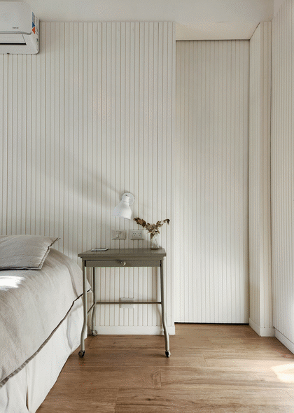 En este lado de la cama, la puerta lleva al baño y el vestidor. Revestimiento de MDF ranurado de Guala Soluciones Decorativas (@gualasd).