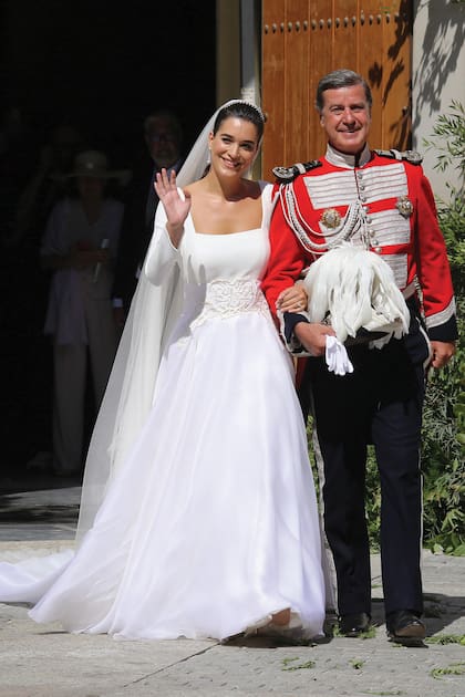 En este plano más amplio de la pareja a la salida de la iglesia, puede apreciarse con detalle qué lucieron en este día tan especial. Por un lado, el duque de Arjona y conde de Salvatierra vistió su uniforme de la Real Maestranza de Caballería de Sevilla. El atuendo está formado por una chaqueta corta con bordados metálicos y pantalón ajustado con galón. Guantes blancos y un bicornio de dos picos completan este equipo que, según la ocasión, puede incluir espada de gala. Por el otro, Bárbara, con un diseño con velo creado por la firma Navascués que tenía, además, unos bordados de la Virgen de las Angustias de la hermandad de los Gitanos. Lució, además, unos pendientes art déco que Cayetano le había regalado especialmente para este momento