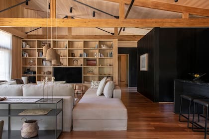 En la casa delteña de la dueña de la tienda de muebles de diseño Solsken, la biblioteca de guatambú se funde con el machimbre de la pared para que en cada nicho se destaquen las piezas decorativas. Sofá ‘Samaná’ en L con funda, almohadones y lámparas tejidas a mano (todo de Solsken).