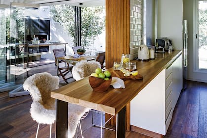 En la cocina, barra desayunadora y de apoyo en petiribí laqueado (De Maderas Norte) con banquetas altas ‘Bertoia’ (Kikely).