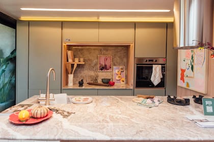En la cocina del espacio "Nexo", de Sara Plazibat, isla con mesada de mármol Fior Di Pesco, muebles en melamina Jade (Faplac) y nicho con mesada y alsada de mármol Silver Galaxy, horno empotrado, nicho retroiluminado.