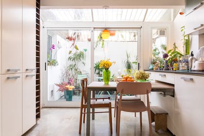 En la cocina, la mesa tipo desayunador está inserta estratégicamente en el mueble de la cocina. Al fondo, el jardín interno de la casa. Silla rosa (Alto Rancho).