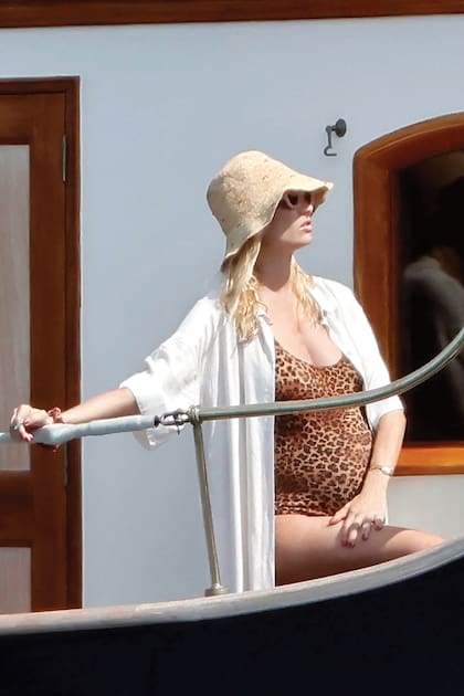 En la cubierta del Pachá III, Beatrice con traje de baño entero de estampa animal, sombrero y anteojos