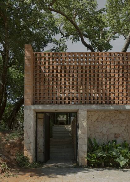En la fachada de esta casa unifamiliar, la piedra conforma la base de la casa, ligada a la tierra por su peso y su comportamiento como muros de contención. Luego vienen los ladrillos, elementos más livianos que permiten un apilamiento y una disposición que organiza los espacios de las plantas superiores.