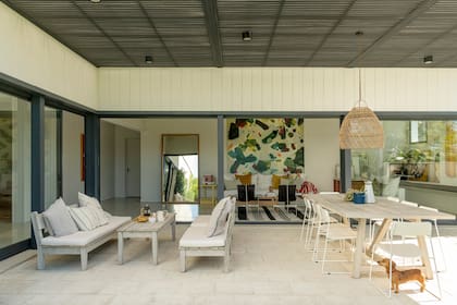 En la galería, acompañando el comedor exterior, un juego de living de Drift Muebles. La mesa de madera rústica es de Wood Market, las sillas de hierro son de un diseño contemporáneo.