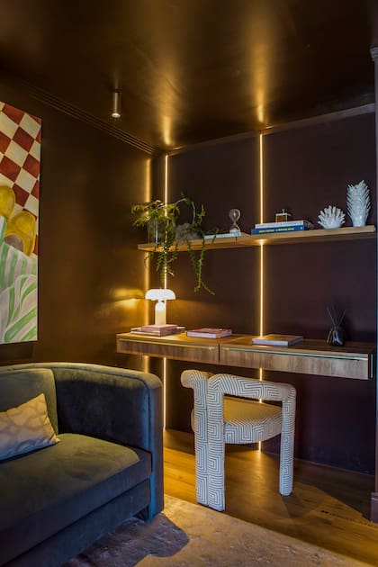 En la oficina, pared entelada de gabardina en tono chocolate que funciona como panel acústico. Sofá color petróleo (Barn). Escritorio y estantes (Mobiline).