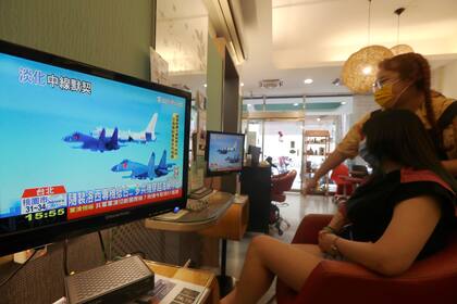 En un salón de belleza en Taipéi, una peluquera y su clienta observan por televisión las maniobras militares chinas en la región (AP Photo/Chiang Ying-ying)