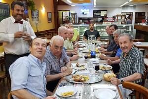 En una mesa larga de un restaurante, muchas personas sentadas alrededor comen milanesas.