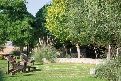 En uno de los laterales, donde los árboles existentes ya tenían cierto tamaño, se ideó un lugar para comer a la sombra y otro de estar, proyectado con un muro bajo de piedra y unos círculos concéntricos que van definiendo el espacio.