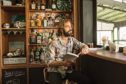 En uno de los rincones del living de su departamento, con libro en mano delante del armario que transformó en bar

