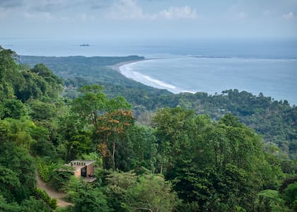 Entre verde profundo y mar infinito, la casa aparece como un refugio mínimo en la ladera.