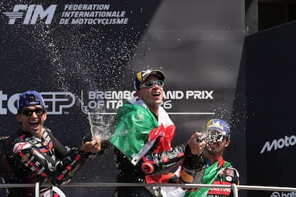 Envuelto en la bandera de Italia, Marco Bezzecchi festeja en el podio junto a Jorge Martín y Francesco Pecco Bagnaia