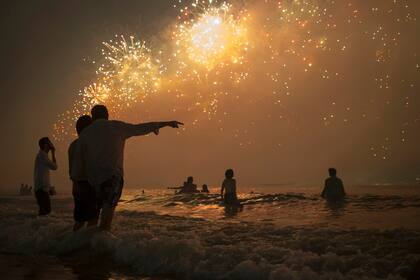 Espectadores miran los fuegos artificiales sobre el océano en la playa de Copacabana, en Rio de Janeiro, Brasil.