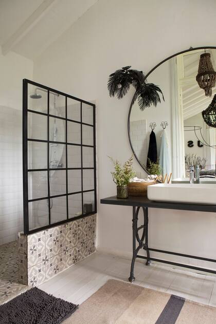 Espejo circular, araña con cuentas y aplique con hojas de hierro (todo de 7-27 Home Collection). Calcareos (Giacomozzi) y mampara de vidrio repartido hasta la altura de los azulejos