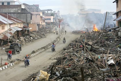 Esta foto combinada creada el 29 de noviembre de 2024 muestra a unos automovilistas pasando junto a los escombros resultantes del tsunami del 26 de diciembre de 2004 que quedaron en la ciudad de Meulaboh, en la provincia de Aceh, el 9 de enero de 2005 (arriba) y en la misma calle el 17 de noviembre de 2024. El 26 de diciembre de 2004, un terremoto de magnitud 9,1 sacudió la costa de Sumatra (Indonesia) y provocó un enorme tsunami en el océano Índico que mató a más de 220.000 personas en una docena de países.
