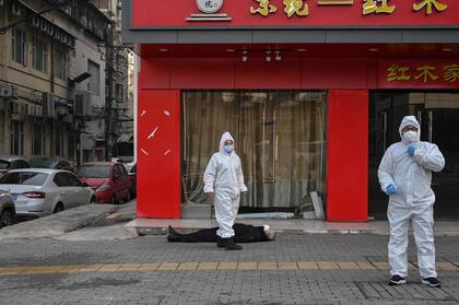 Esta foto de archivo tomada el 30 de enero de 2020 muestra a funcionarios con trajes protectores revisando a un anciano con mascarilla que se desplomó y murió en una calle cerca de un hospital en Wuhan, provincia central china de Hubei.