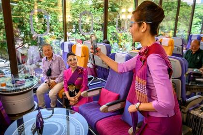 Esta foto tomada el 10 de septiembre de 2020 muestra a una asistente de vuelo de Thai Airways con un protector facial mientras ayuda a un cliente a tomar una foto con un teléfono móvil en un restaurante con temática de avión en la sede de la aerolínea en Bangkok