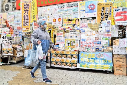 Esta foto tomada el 15 de marzo de 2024 muestra a una mujer pasando por una tienda cubierta de publicidad a lo largo de una calle comercial en el centro de Osaka.