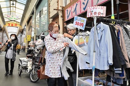 Esta foto tomada el 15 de marzo de 2024 muestra a compradores con barbijo probándose ropa de segunda mano a la venta en una calle comercial de Osaka.