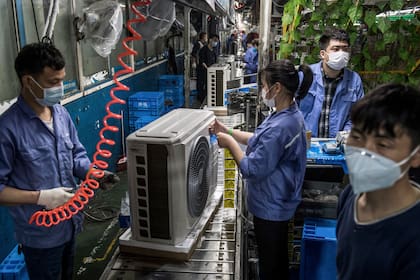 Esta foto tomada el 25 de marzo de 2020 muestra a los empleados que trabajan en una línea de producción de aire acondicionado en una fábrica de Midea en Wuhan, en la provincia central china de Hubei