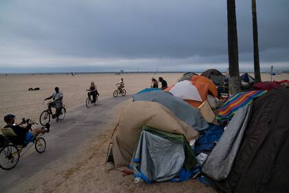 Esta fotografía del 29 de junio de 2021 muestra a varias personas paseando en bicicleta frente a un campamento de indigentes en Los Ángeles. (AP Foto/Jae C. Hong, Archivo)