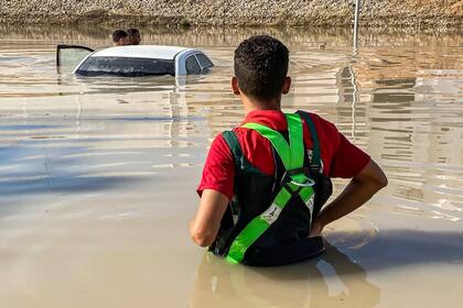 Esta fotografía publicada en la cuenta de la Media Luna Roja Libia en la plataforma X (anteriormente Twitter) el 14 de septiembre de 2023 muestra a un miembro de pie en una zona inundada cerca de un vehículo sumergido tras las inundaciones tras la tormenta mediterránea " Daniel" atacó la ciudad de Derna