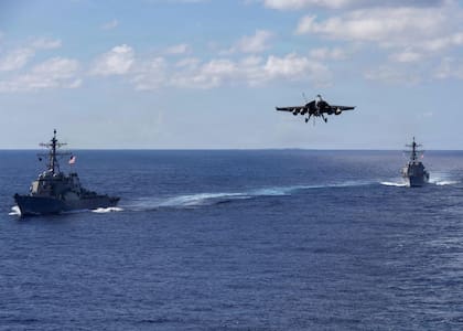 Esta imagen del Departamento de Defensa de EE.UU. muestra a los destructores de misiles guiados clase Arleigh Burke USS Mahan (DDG 72), a la izquierda, y USS Bainbridge (DDG 96) navegando en formación mientras un F/A-18 Super Hornet, asignado al Carrier Air Wing Eight embarcado a bordo del USS Gerald R. Ford (CVN 78), desciende en la aproximación final para aterrizar en el portaaviones el 13 de noviembre de 2025 en un lugar no revelado en el Océano Atlántico.