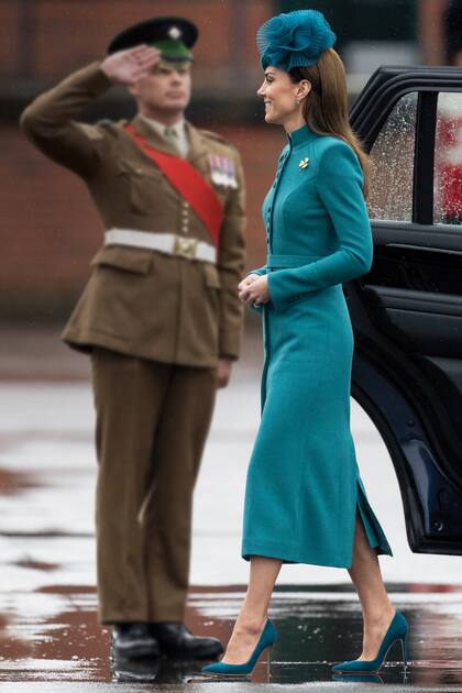 Este año, en Mons Barracks, Aldershot, la princesa de Gales optó por un vestido-abrigo midi turquesa, con hombros marcados, cuello mao y botones –agrupados de a cuatro, como los uniformes militares– de Catherine Walker, stilettos 105 de Gianvito Rossi en tonalidad Persian y tocado de Jane Taylor (modelo Clio). El broche que llevó sobre su tapado es el trébol de la Guardia Irlandesa y fue realizado por Cartier para la princesa María, tía de la reina Isabel II, en 1961, cuatro años antes de su muerte.