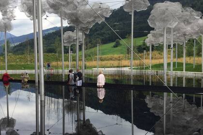 Estructura de hierro sostienen nubes de metal que se reflejan en un gran espejo de agua. Las nubes, a su vez, sostienen cristales que asemejan gotas de agua