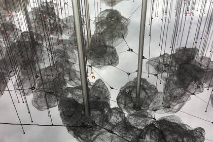 Estructura de hierro sostienen nubes de metal que se reflejan en un gran espejo de agua. Las nubes, a su vez, sostienen cristales que asemejan gotas de agua