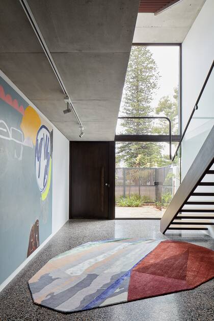 Excepto por el garage, la planta baja solo aloja la escalera que une verticalmente la casa. Un riel con apliques de porcelana (Michael Anastassiades) ilumina la obra de Elle Campbell. La alfombra ‘Fordite’ es una creación de Patricia Urquiola para CC-Tapis.