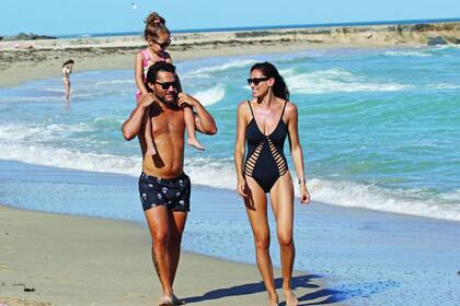 Familia feliz. Nina es la gran debilidad de los dos: papá la lleva a caballito sobre los hombros y mamá la peina y la lookea. Con un traje de baño negro con tiras laterales, Debora luce por la playa sus curvas de infarto.