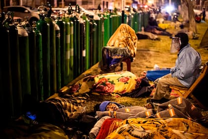 Familiares de pacientes con Covid-19 esperan durante la noche para realizar la recarga de los tubos de oxígeno, en Callao, Perú