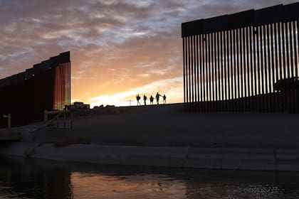 Familias migrantes pasan por un hueco en la valla fronteriza de Estados Unidos en Yuma, Arizona (AP Foto/Eugene Garcia, Archivo)