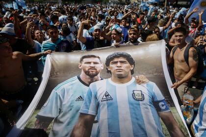 Fans of Argentina hold a flag depicting Argentine football stars Lionel Messi (L) and late Diego Maradona (R) while gathering at the Obelisk to celebrate winning the Qatar 2022 World Cup against France in Buenos Aires, on December 18, 2022. (Photo by Emiliano Lasalvia / AFP)